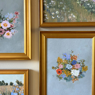 Four framed paintings of floral and landscape scenes on a wall.